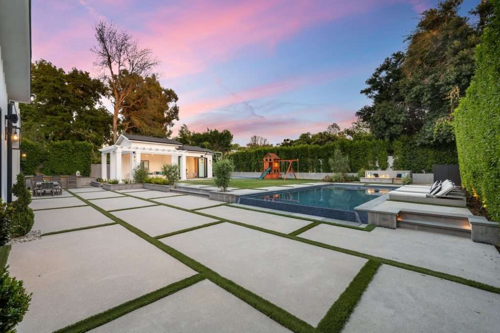 a backyard that has concrete pavers and a pool with grass surrounding it